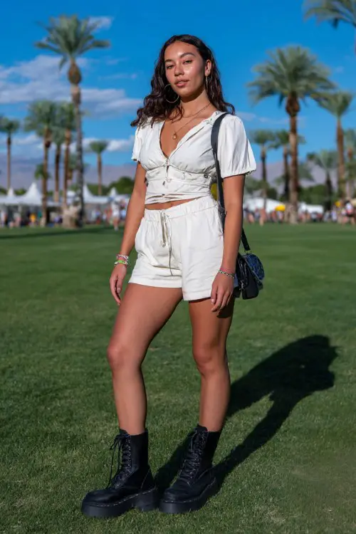 a woman wears a white crop top with shorts, black boots and black bag