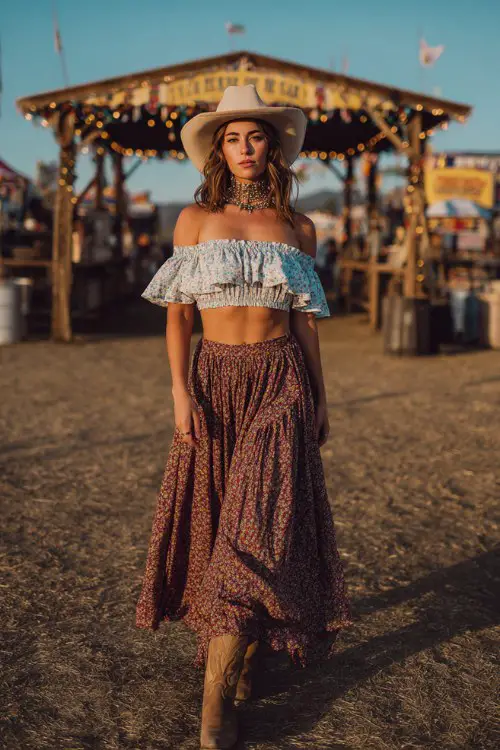 woman wearing an off-shoulder ruffle crop top with a layered bohemian maxi skirt, cowboy hat, statement necklace, cowboy boots