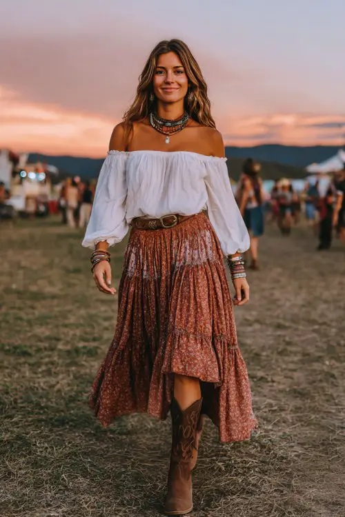 woman wears an off-shoulder white peasant blouse with billowy sleeves, layered bohemian skirt in rust and cream tones, and brown cowboy boots
