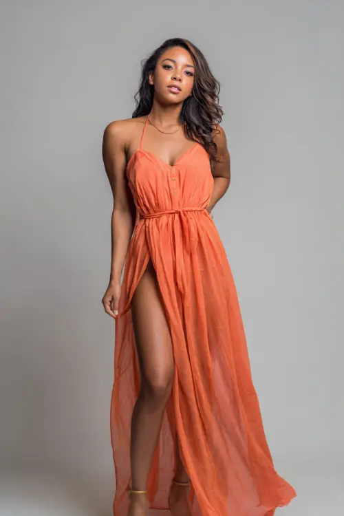 A woman wearing a flowy chiffon maxi dress with a thigh-high slit and block heels, styled for an elegant summer evening, simple studio background 