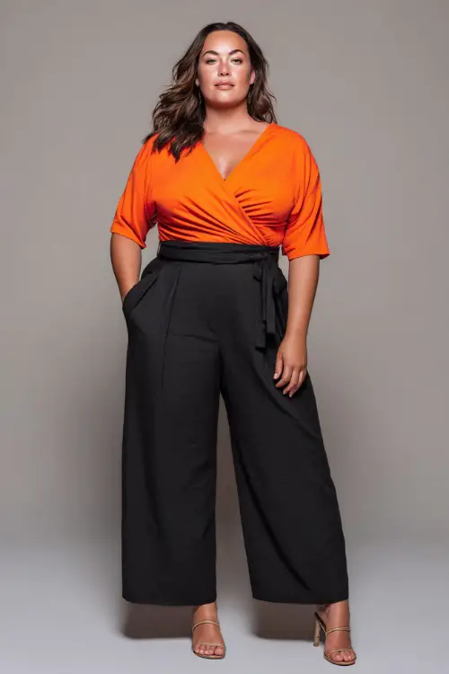 A plus-size woman wearing a bright orange wrap top with high-waisted wide-leg trousers and open-toe heels, styled for a bold and flattering summer night look 