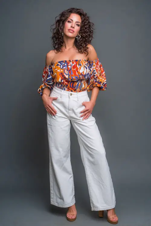 A woman in a bold printed blouse with white wide-leg jeans and platform heels, styled for a stylish summer evening in NYC, simple studio background 