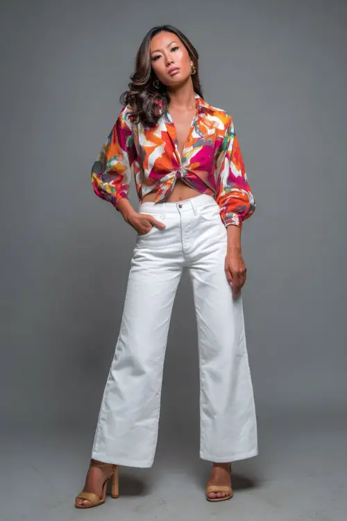 A woman in a bold printed blouse with white wide-leg jeans and platform heels, styled for a stylish summer evening in NYC, simple studio background
