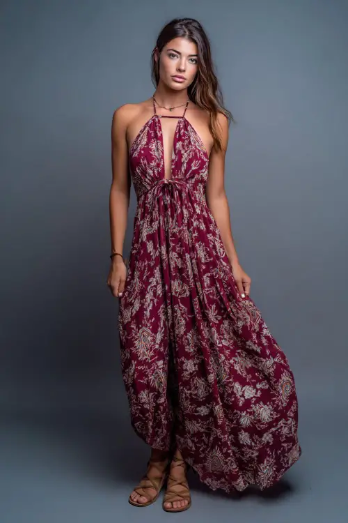 A woman in a flowy halter maxi dress with a low back and flat sandals, styled for a boho-inspired summer bar night, simple studio background 