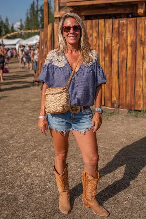 A woman over 40 dressed in high-rise denim shorts, a tucked-in peasant blouse with lace details, and tan cowgirl boots