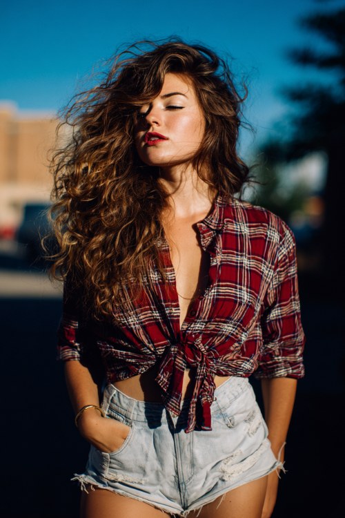 Curvy country concert look with tied-up plaid shirt, cutoff shorts, and messy waves, carefree and sunlit