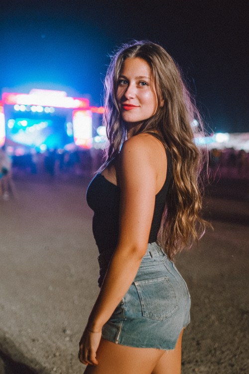 curvy woman in a black bodysuit, high-waisted denim shorts, and cowboy boots, nighttime country concert lights