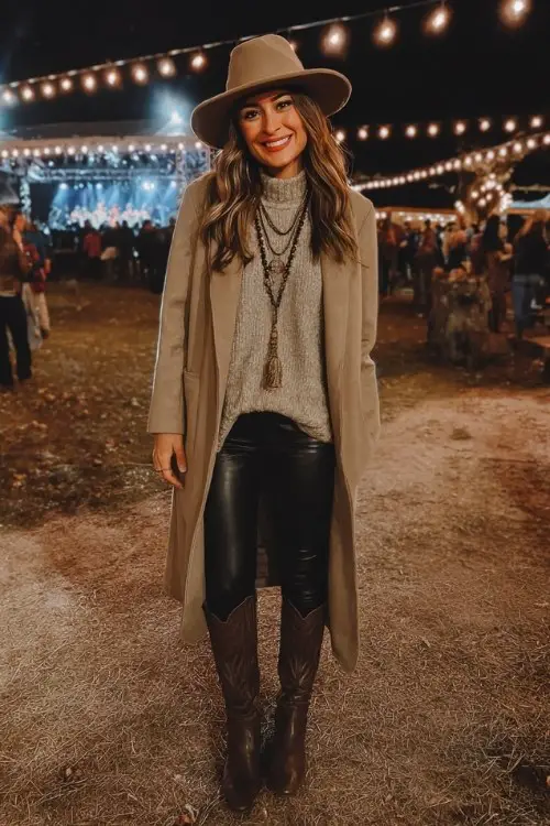 A woman dressed in a long tan wool coat over a knit turtleneck sweater, black faux leather leggings, and tall western-style cowboy boots