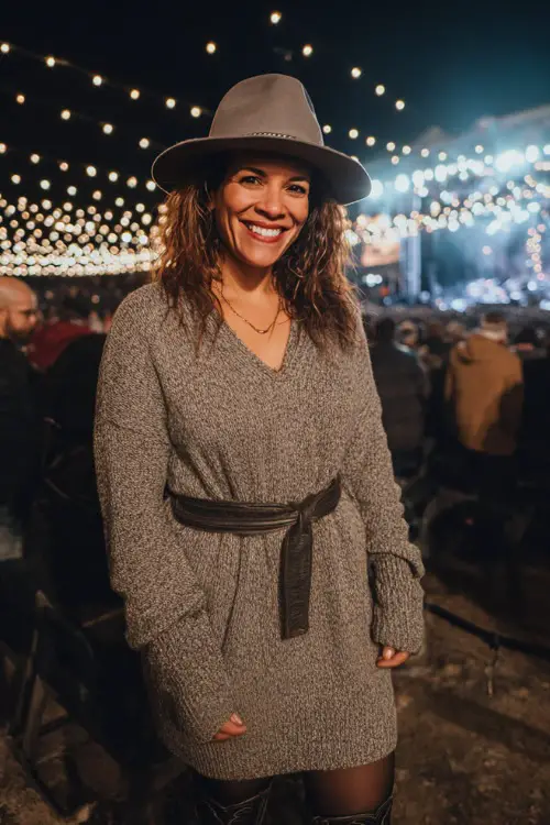 A woman over 40 wears a long sleeve knit sweater dress with a belted waist, black tights, and tall cowboy boots 