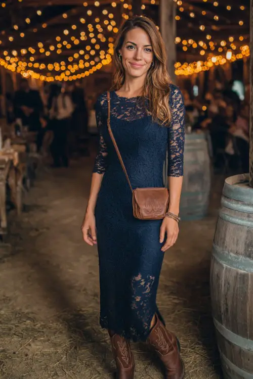 A woman wears a navy blue lace midi dress with three-quarter sleeves, styled with brown Western boots and a leather crossbody bag