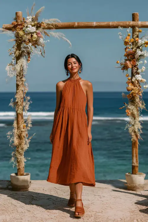A woman wears a rust-orange sleeveless midi dress with a pleated skirt, paired with block heel sandals and minimal jewelry 