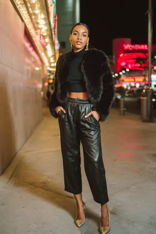 A fashionable Black woman in a cropped faux fur jacket worn over a sleek turtleneck top, paired with high-waisted leather pants and pointed-toe heels