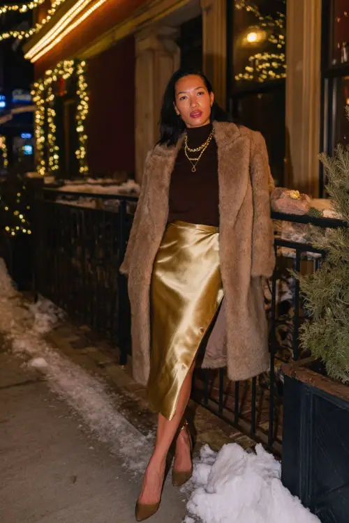 A fashionable woman in a satin midi skirt paired with a fitted turtleneck and pointed heels, layered with a long coat 