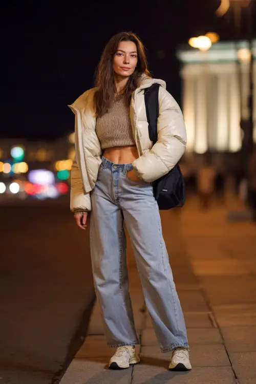 A stylish woman wearing wide-leg jeans with a cropped sweater and a short puffer jacket, accessorized with a mini backpack