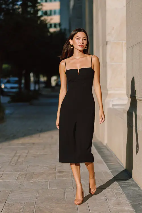 A woman wearing a slip-style midi dress in a neutral tone layered with a lightweight cardigan, styled with minimalist sandals