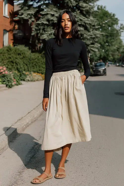A woman wearing a simple black long-sleeve top tucked into a flowy neutral midi skirt, styled with minimalist sandals 
