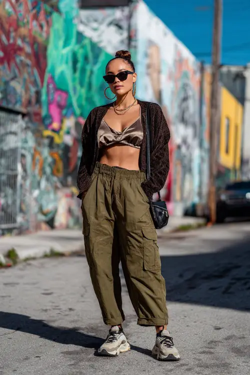 confident woman wearing a cropped cardigan over a satin cami top with oversized cargo pants and chunky sneakers 