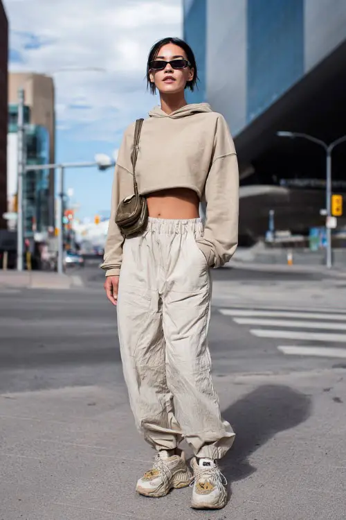 confident woman wearing a cropped hoodie with low-rise parachute pants and chunky sneakers, accessorized with a small shoulder bag and sporty sunglasses, Y2K streetwear outfit