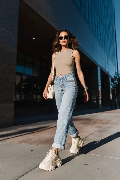 confident woman wearing a fitted baby tee with low-rise straight-leg jeans and chunky platform sneakers, accessorized with a baguette bag and tinted sunglasses 