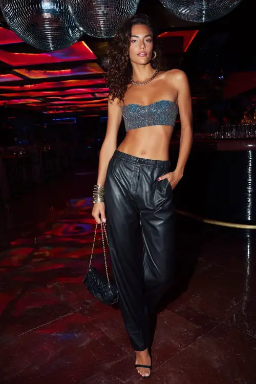 confident woman wearing a glittery tube top with low-rise leather pants and sleek high heels, accessorized with chunky bracelets and a mini shoulder bag, bold Y2K club outfit with heels