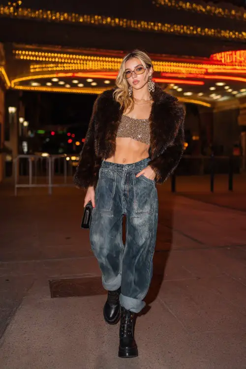 fashionable woman wearing a cropped faux fur jacket over a glittery crop top with oversized baggy jeans and platform boots, accessorized with statement earrings and a mini bag
