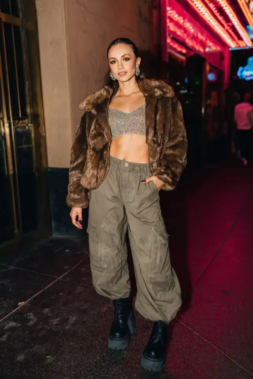 fashionable woman wearing a cropped faux fur jacket over a glittery crop top with oversized cargo pants and platform boots, accessorized with statement earrings and a mini bag 