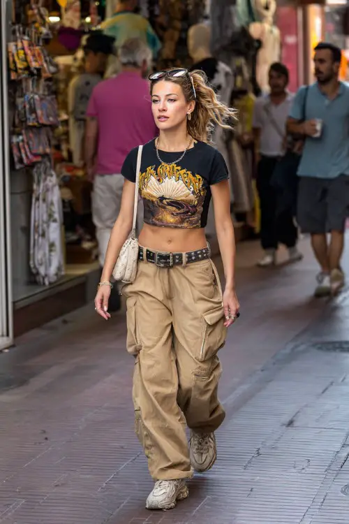 fashionable woman wearing a graphic baby tee tucked into low-rise cargo pants with a statement belt and chunky sneakers, accessorized with a shoulder bag and hair clips 