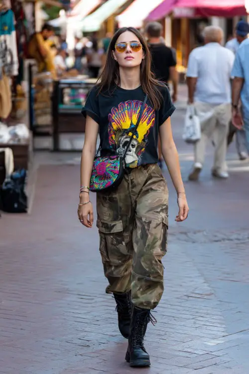 fashionable woman wearing a graphic baby tee with low-rise cargo pants and chunky boots, accessorized with a colorful shoulder bag and tinted sunglasses, edgy Y2K outfit with boots