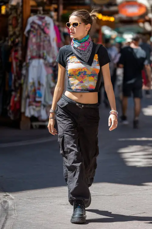 fashionable woman wearing a graphic baby tee with low-rise cargo pants and chunky platform sneakers, accessorized with a colorful bandana and tinted sunglasses, edgy Y2K outfit with bandana