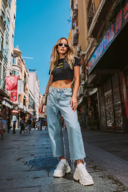 fashionable woman wearing a rhinestone baby tee with low-rise bootcut jeans, chunky platform sneakers and a small shoulder bag, classic 2000s Y2K outfit