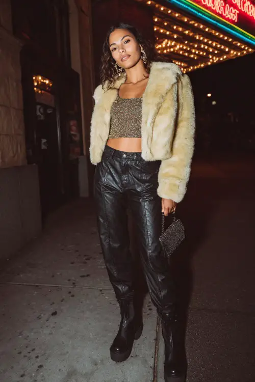 stylish woman wearing a cropped faux fur jacket over a glittery crop top with low-rise leather-accent jeans and platform boots