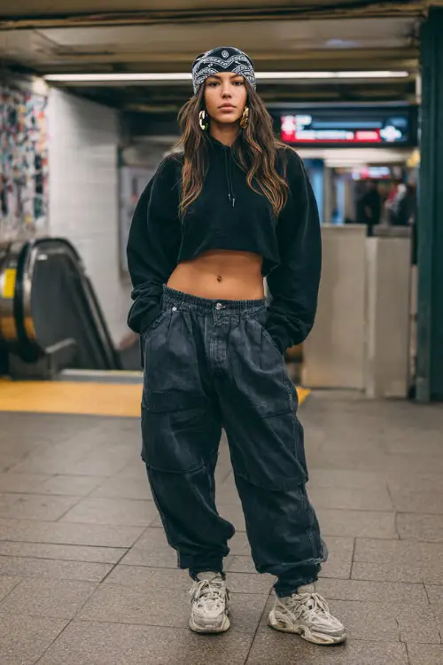 stylish woman wearing a cropped hoodie with baggy jeans and chunky sneakers, accessorized with a printed bandana tied over her hair and hoop earrings, sporty Y2K streetwear outfit with bandana