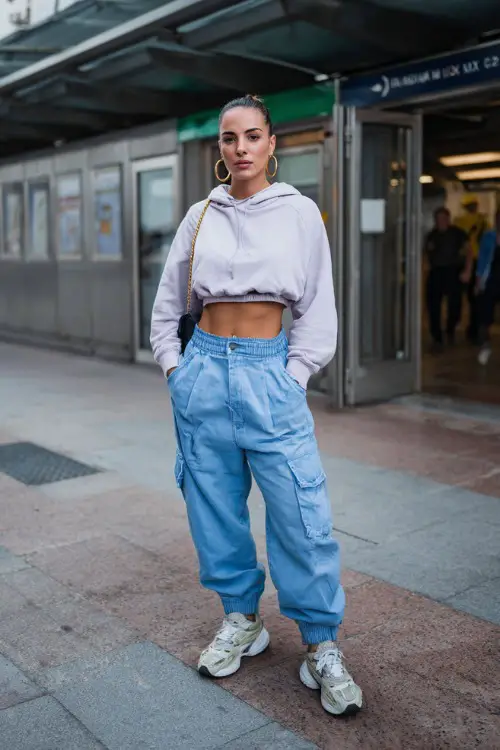stylish woman wearing a cropped hoodie with extra-wide baggy jeans and chunky sneakers, accessorized with hoop earrings and a mini handbag, sporty Y2K streetwear outfit with baggy jeans