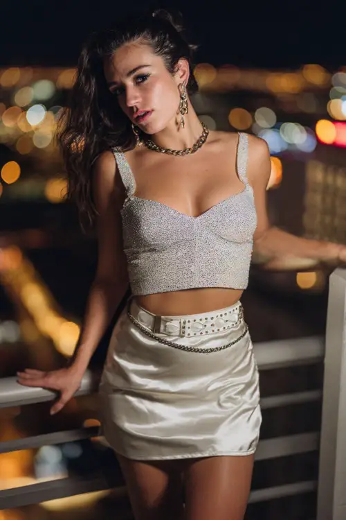 stylish woman wearing a glittery crop top with a satin mini skirt and a chain belt, paired with strappy heels and statement earrings, glamorous Y2K party outfit with belt