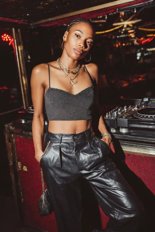 stylish woman wearing a glittery tube top with low-rise leather pants and tall platform boots, accessorized with layered necklaces and a mini baguette bag, bold early 2000s club fashion
