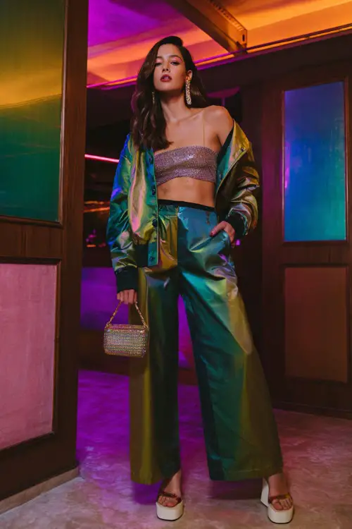 stylish woman wearing a shiny satin jacket over a glittery tube top with low-rise wide-leg pants and platform heels, accessorized with statement earrings and a mini bag 