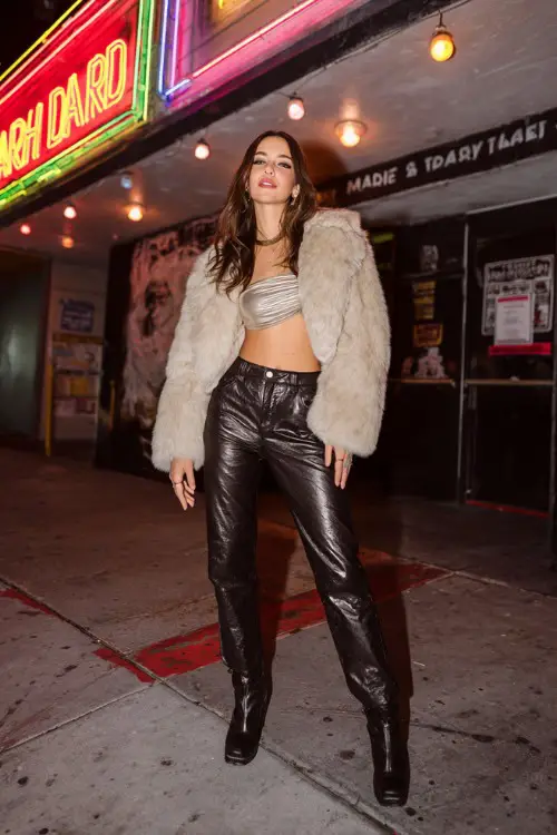 trendy woman wearing a cropped faux fur jacket over a shiny tube top and low-rise leather pants with platform boots, Y2K club fashion vibe 