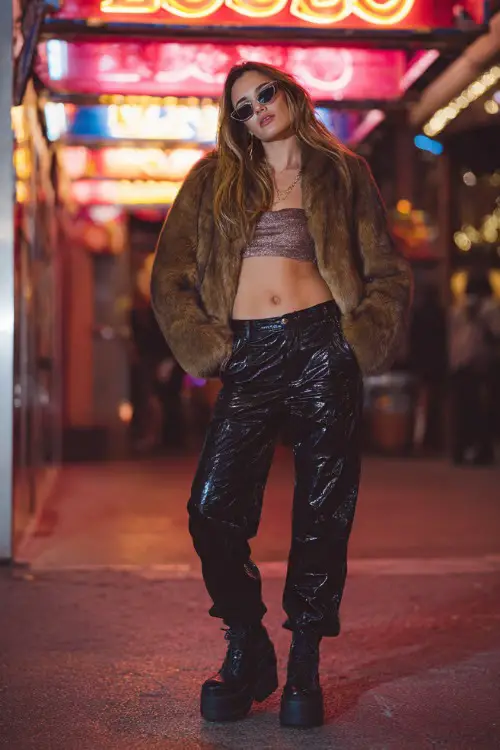 trendy woman wearing a cropped faux fur jacket over a shiny tube top and low-rise leather pants with platform boots, Y2K club fashion vibe