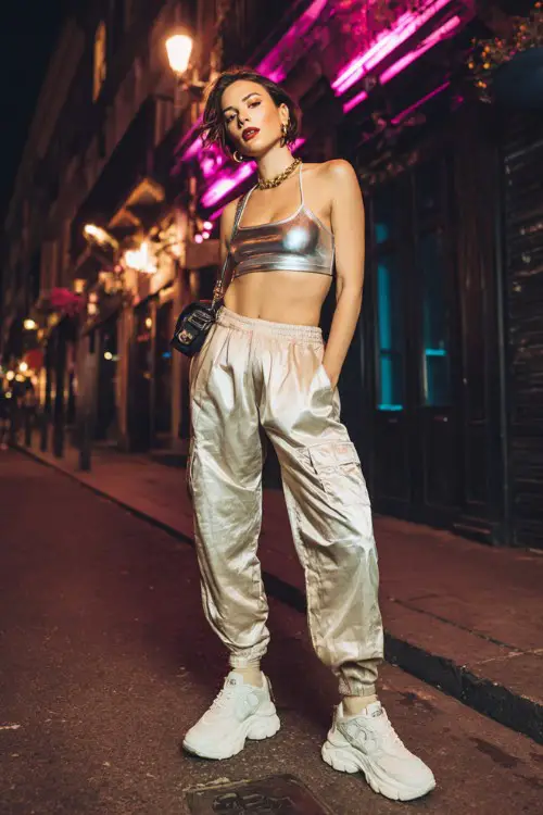 trendy woman wearing a metallic crop top with low-rise cargo pants and chunky platform sneakers, accessorized with hoop earrings and a mini bag, edgy Y2K club street style