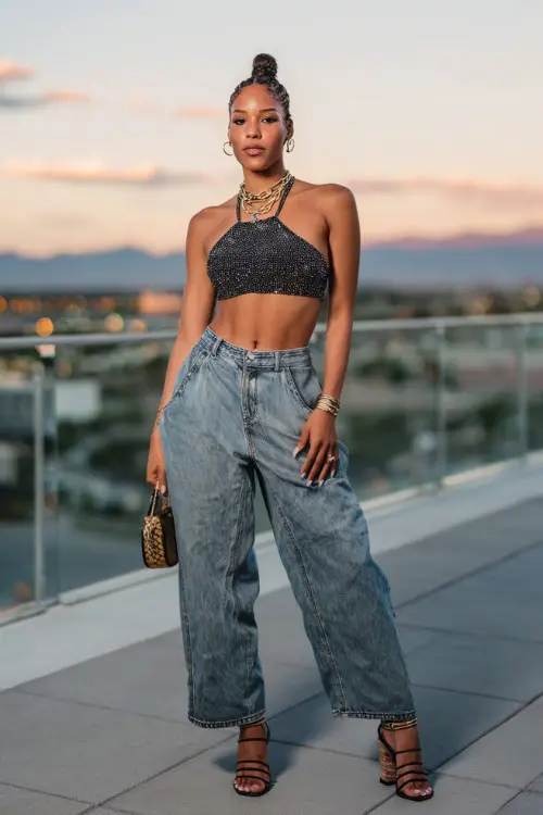 trendy woman wearing a sparkly halter crop top with baggy jeans and strappy heels, accessorized with layered necklaces and a baguette bag, Y2K party outfit with baggy jeans 