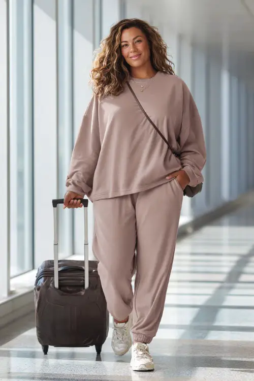 A plus-size woman wears a soft matching lounge set with an oversized sweatshirt and tapered jogger pants, paired with sleek sneakers and a crossbody bag 