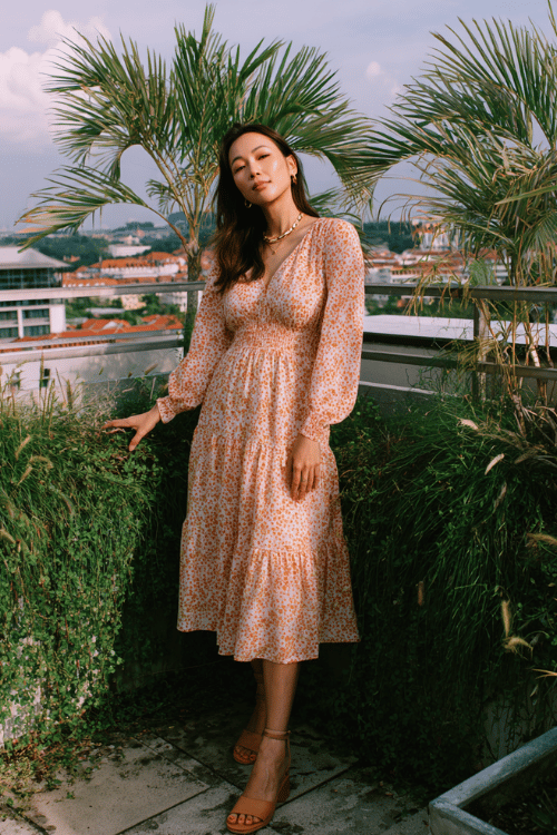 a radiant woman in her 30s wearing a feminine floral printed long-sleeve midi dress in warm peach and cream with a smocked bodice and tiered skirt