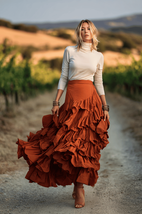 a striking woman in her 40s wearing a dramatic tiered ruffle maxi skirt in terracotta paired with a fitted long-sleeve mock-neck top in ivory 