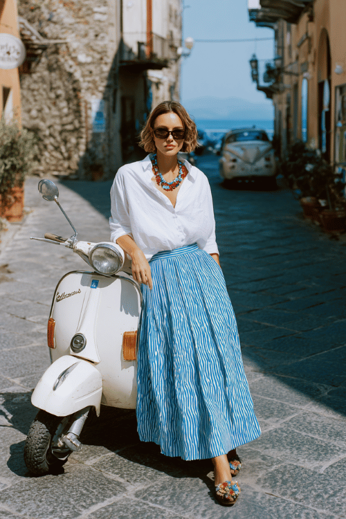 bold woman wearing a crisp white oversized button-down shirt tucked into a flowing pleated midi skirt in ocean blue with subtle wave-print pattern