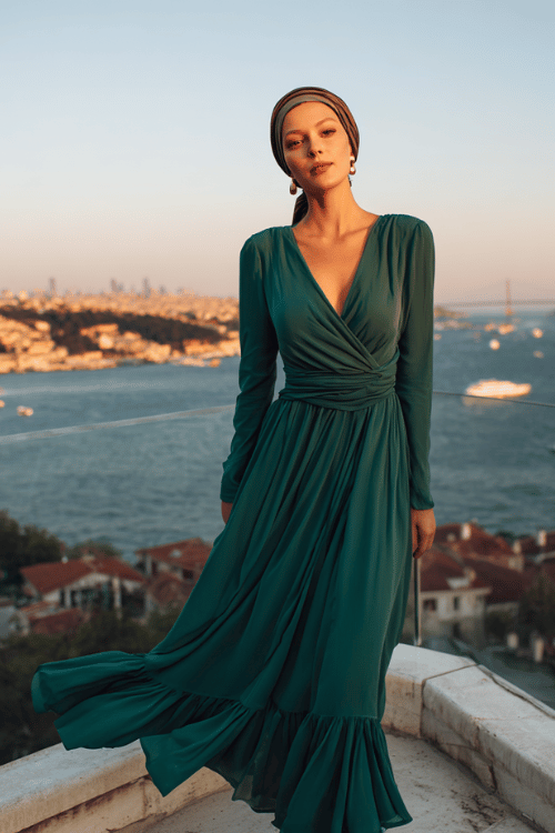 elegant woman wearing a sophisticated long-sleeve chiffon maxi dress in deep emerald green with a softly draped cowl neckline and fluttering skirt panels