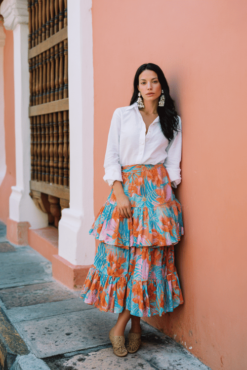 woman wearing a tiered cotton midi skirt in vibrant tropical print paired with a crisp white long-sleeve linen shirt tucked in at the front