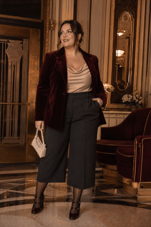 Plus-size woman wearing a burgundy velvet blazer with a champagne satin top and black wide-leg culottes.