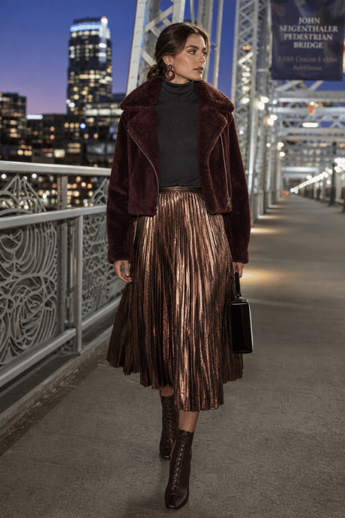 Woman in a burgundy faux fur jacket with a metallic pleated midi skirt and lace-up ankle boots.