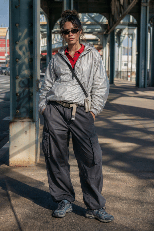 Woman in a silver windbreaker, red polo shirt, gray cargo pants, and chunky sneakers.