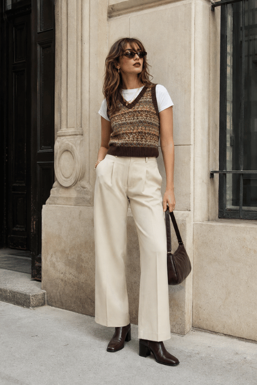 Woman wearing a Fair Isle sweater vest with cream wide leg trousers and brown ankle boots.